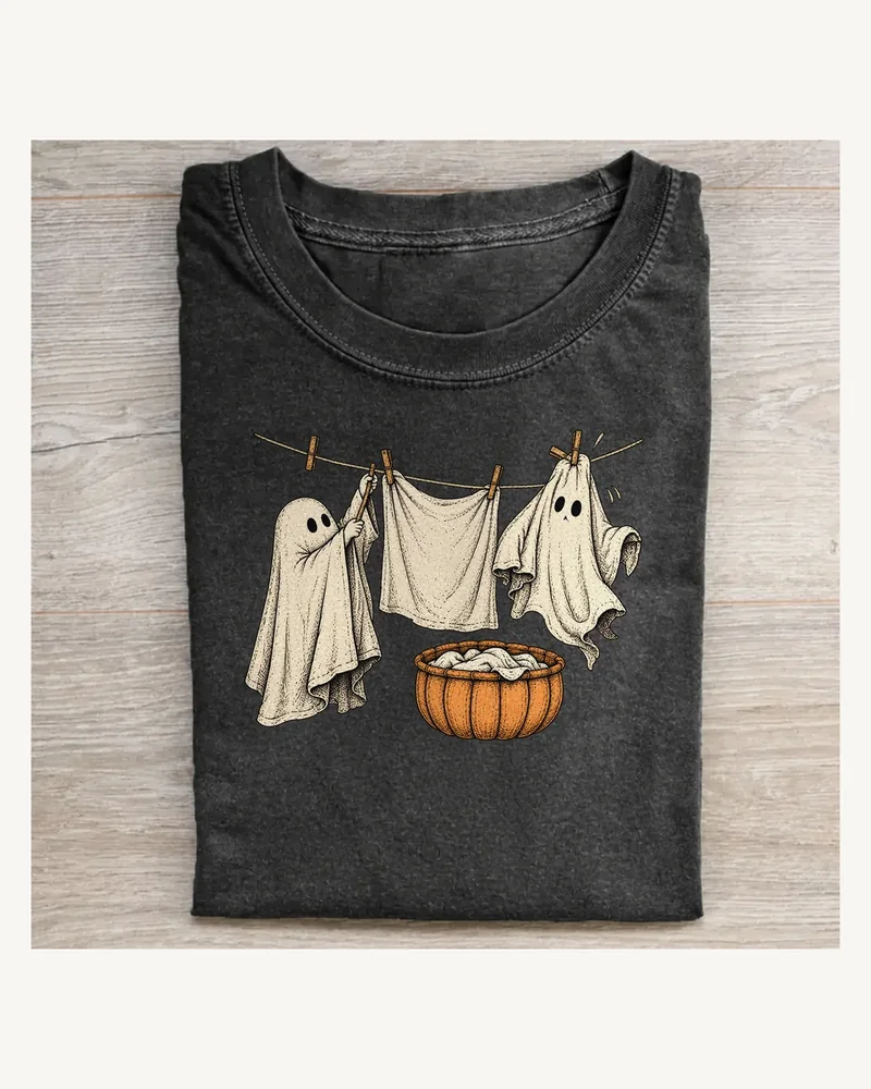Folded washed black T-shirt featuring Ghost Laundry Night on a pale wood tabletop