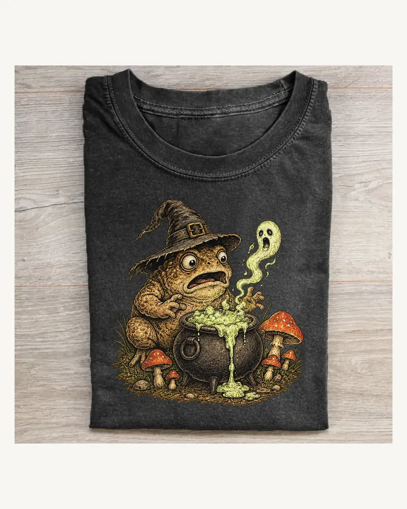 Folded washed black T-shirt featuring Potion Spill on a pale wood tabletop