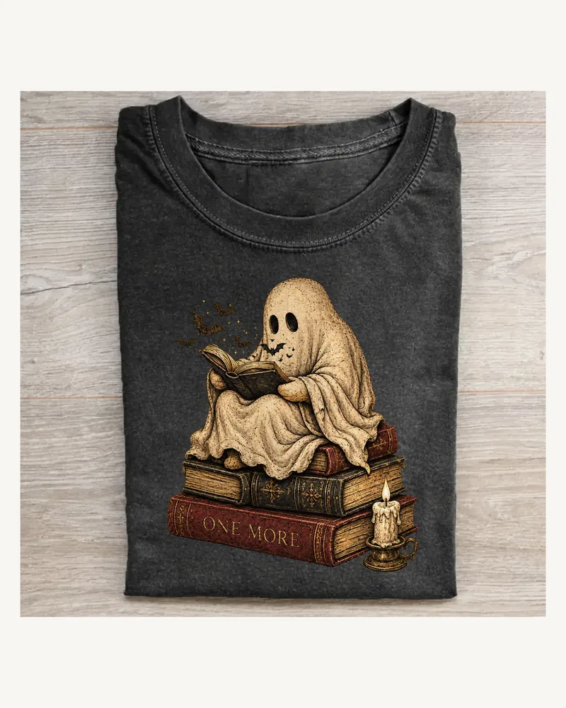 Folded washed black T-shirt featuring One More Chapter on a pale wood tabletop