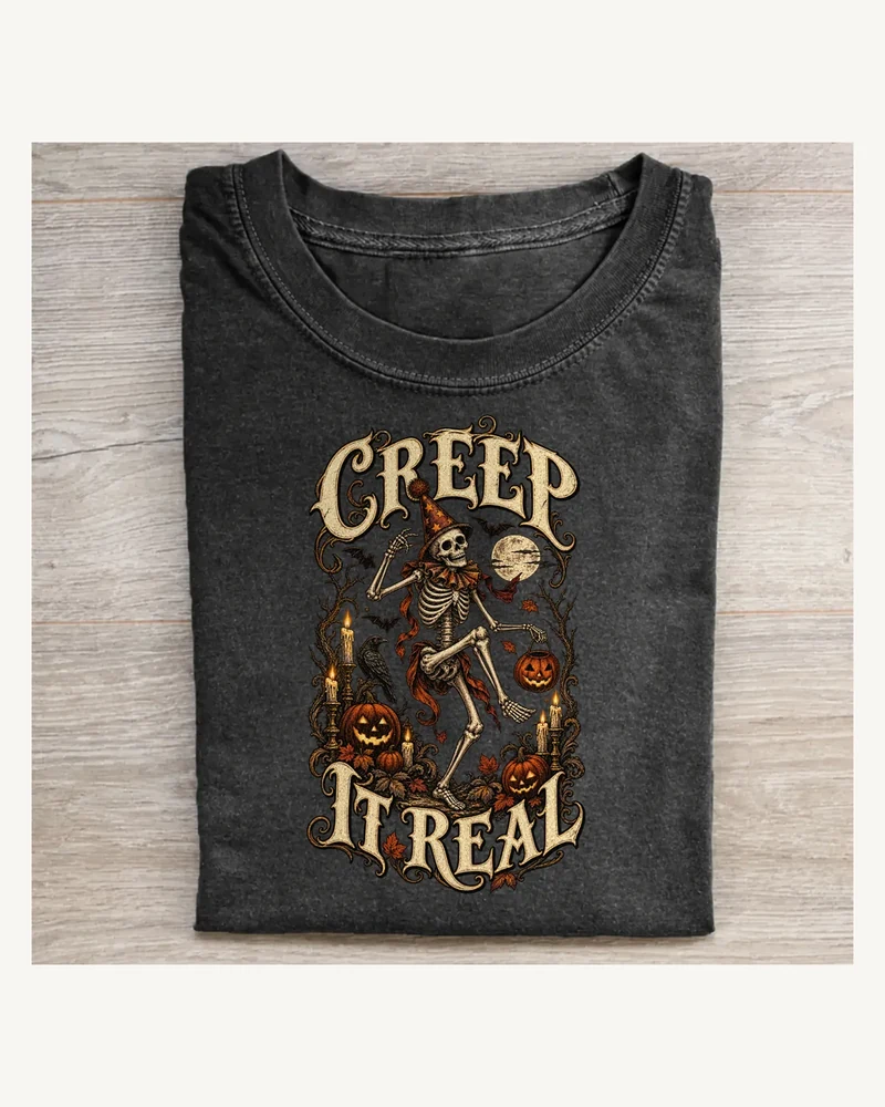 Folded washed black T-shirt featuring CREEP IT REAL gothic lettering and Halloween artwork