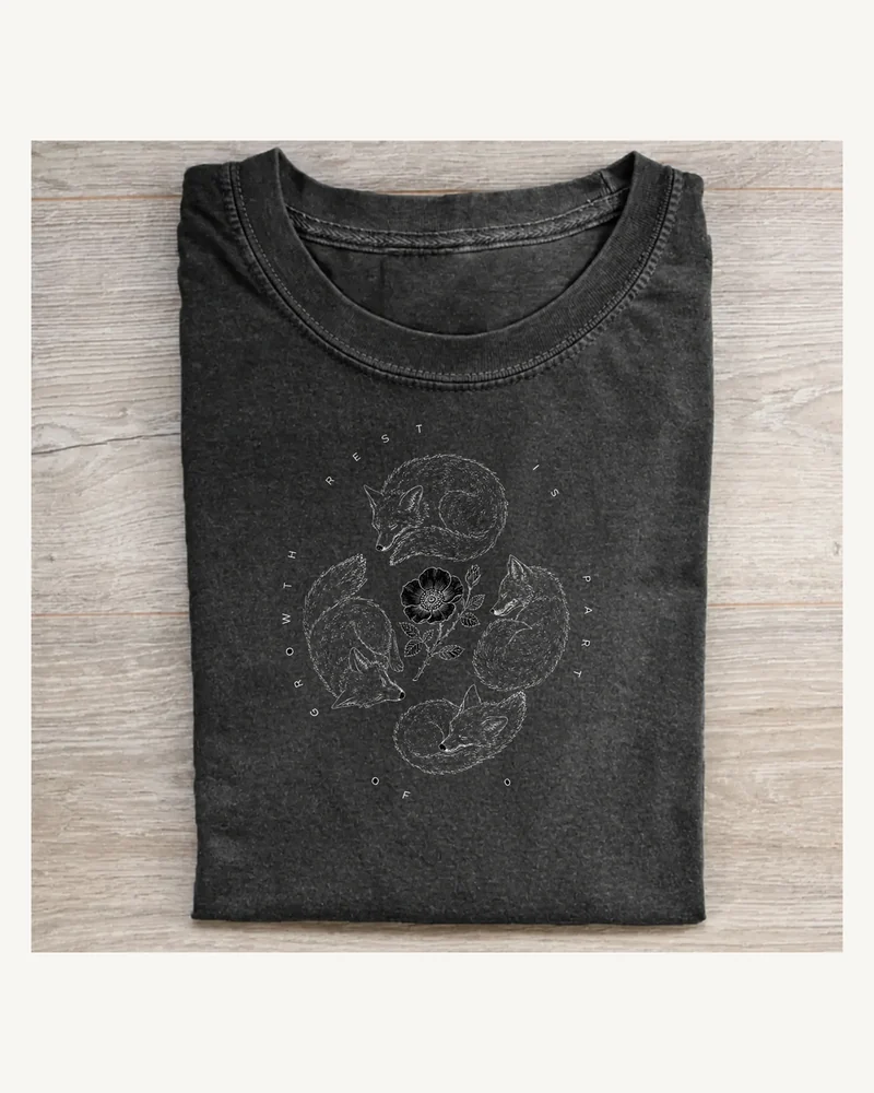 Folded charcoal cotton T-shirt with three resting cats circling a small flower in monochrome linework
