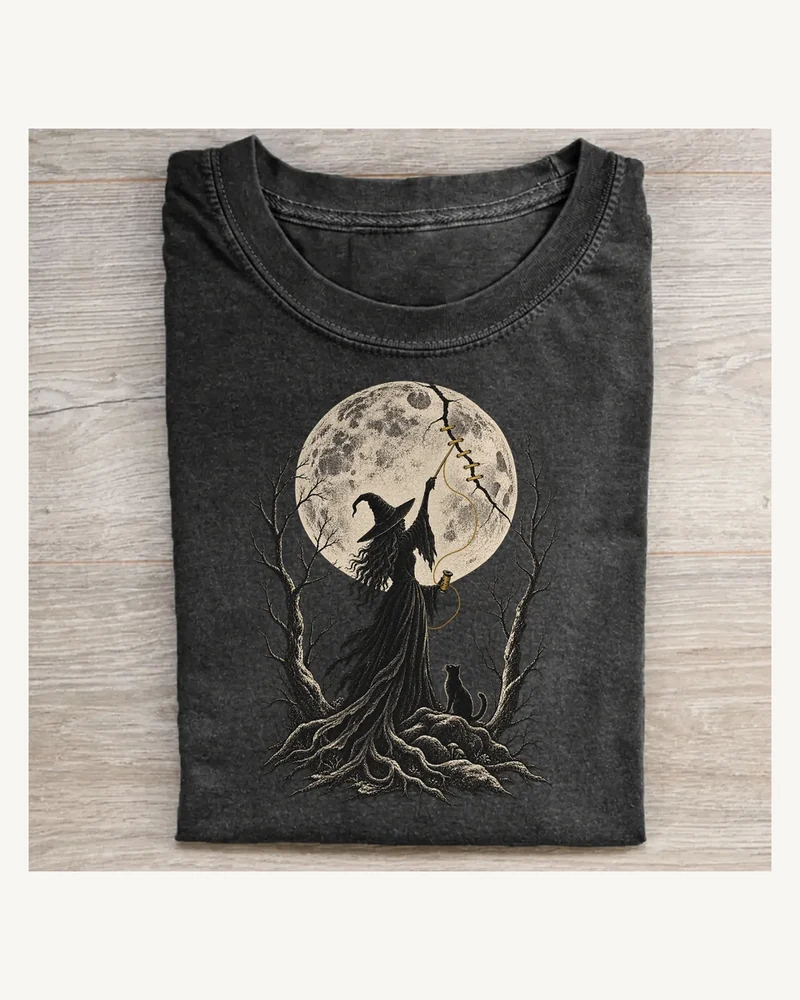 Folded washed black T-shirt featuring Moon Mender moonlit witch artwork