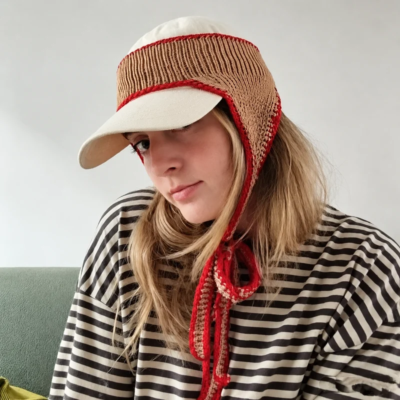 Tan ribbed knit ear warmer headband with red edging styled over a cream cap